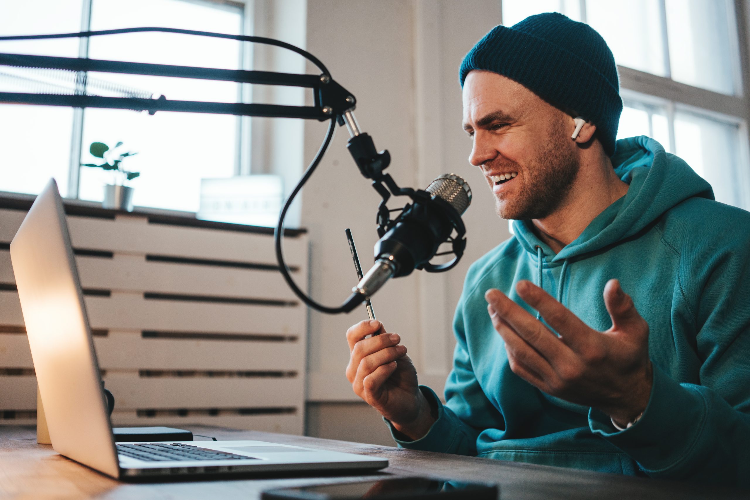 Cheerful host with stubble streaming his audio podcast using microphone and laptop at his small broadcast studio